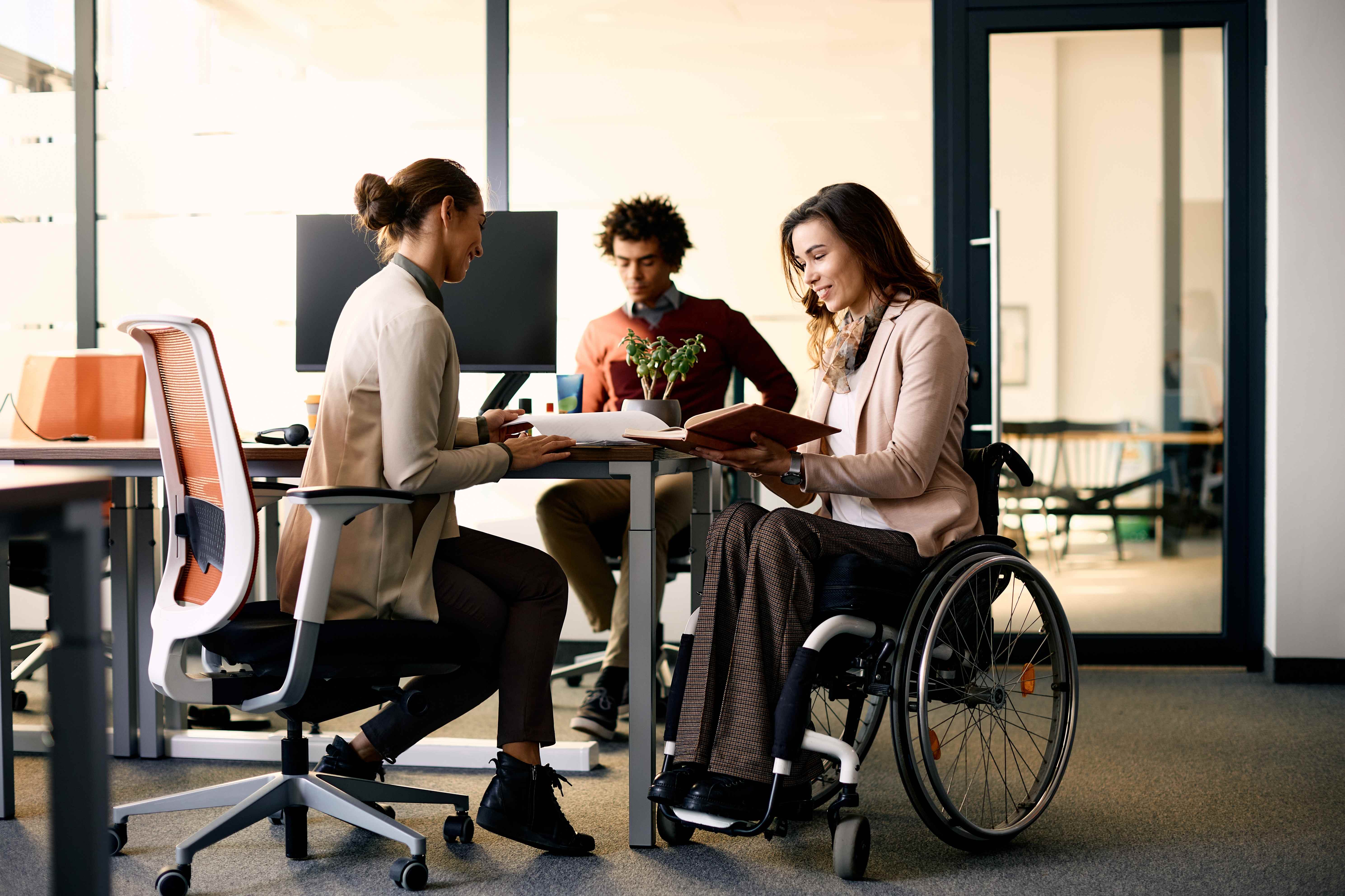 Professional woman in wheelchair working confidently with colleagues in modern office environment