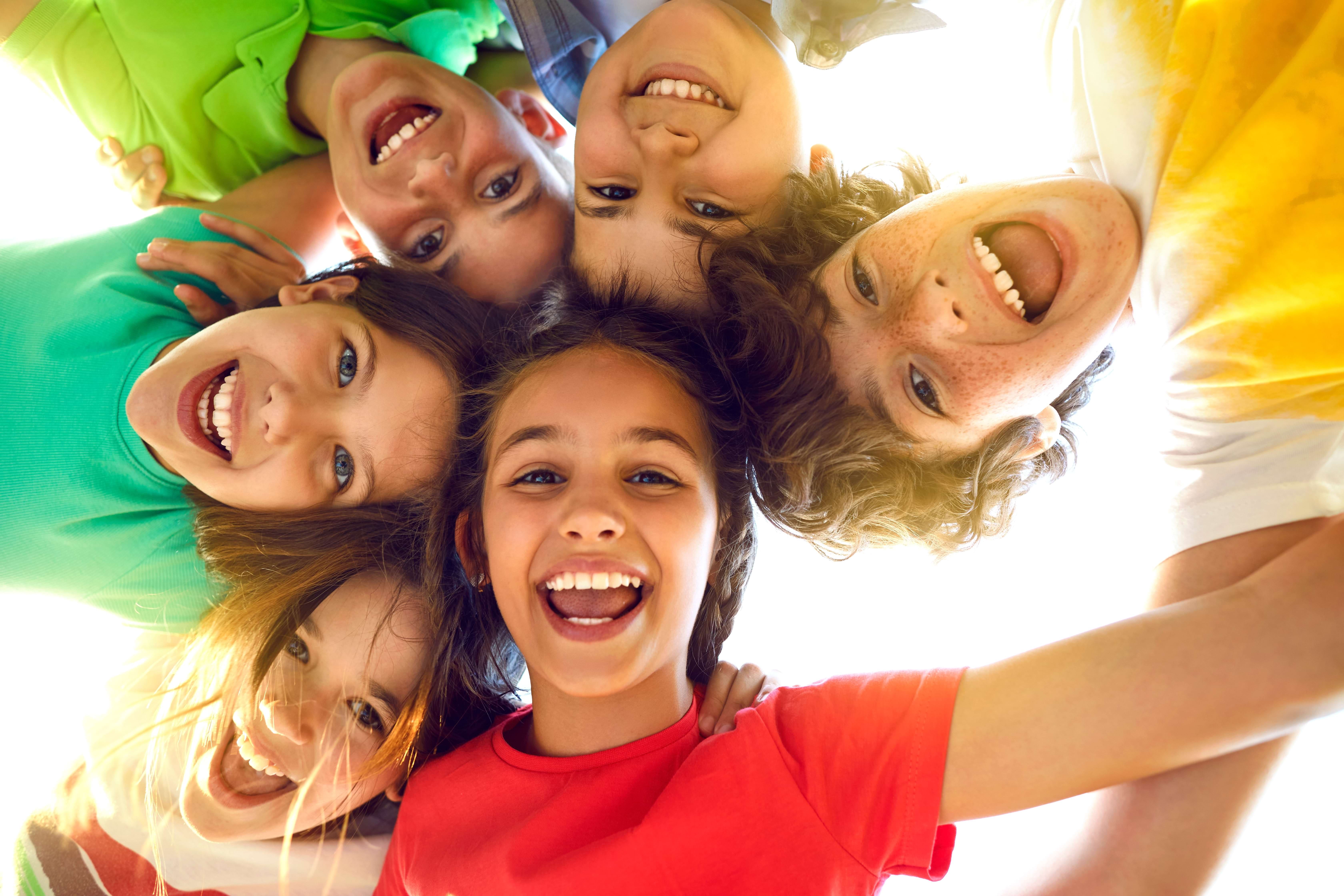 Happy diverse group of children in a circle looking down at camera, smiling joyfully - representing the positive outcomes of early childhood intervention