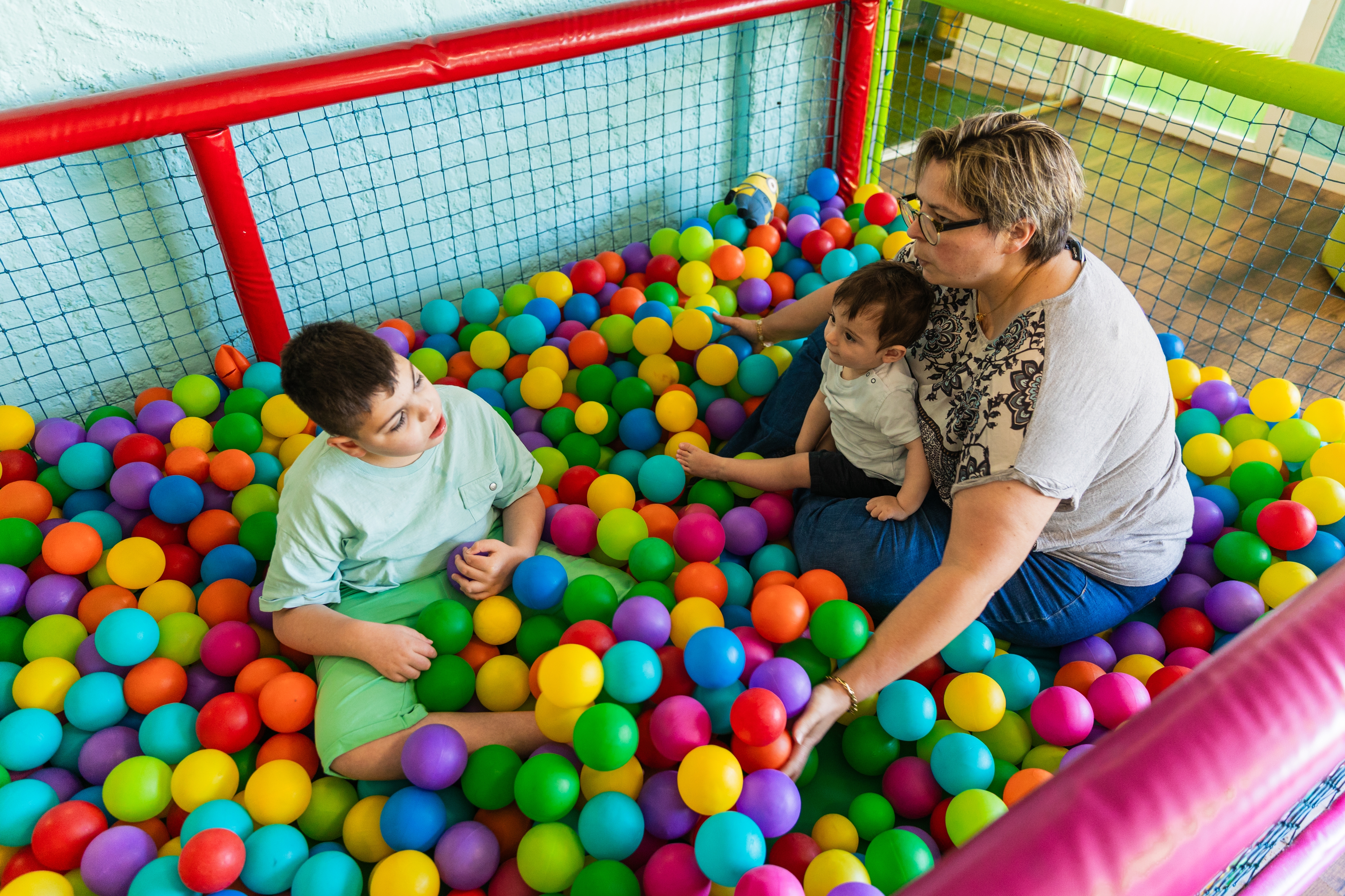 Therapist working with very young children (ages 0-9) in colorful sensory ball pit environment, representing early childhood intervention and therapeutic play